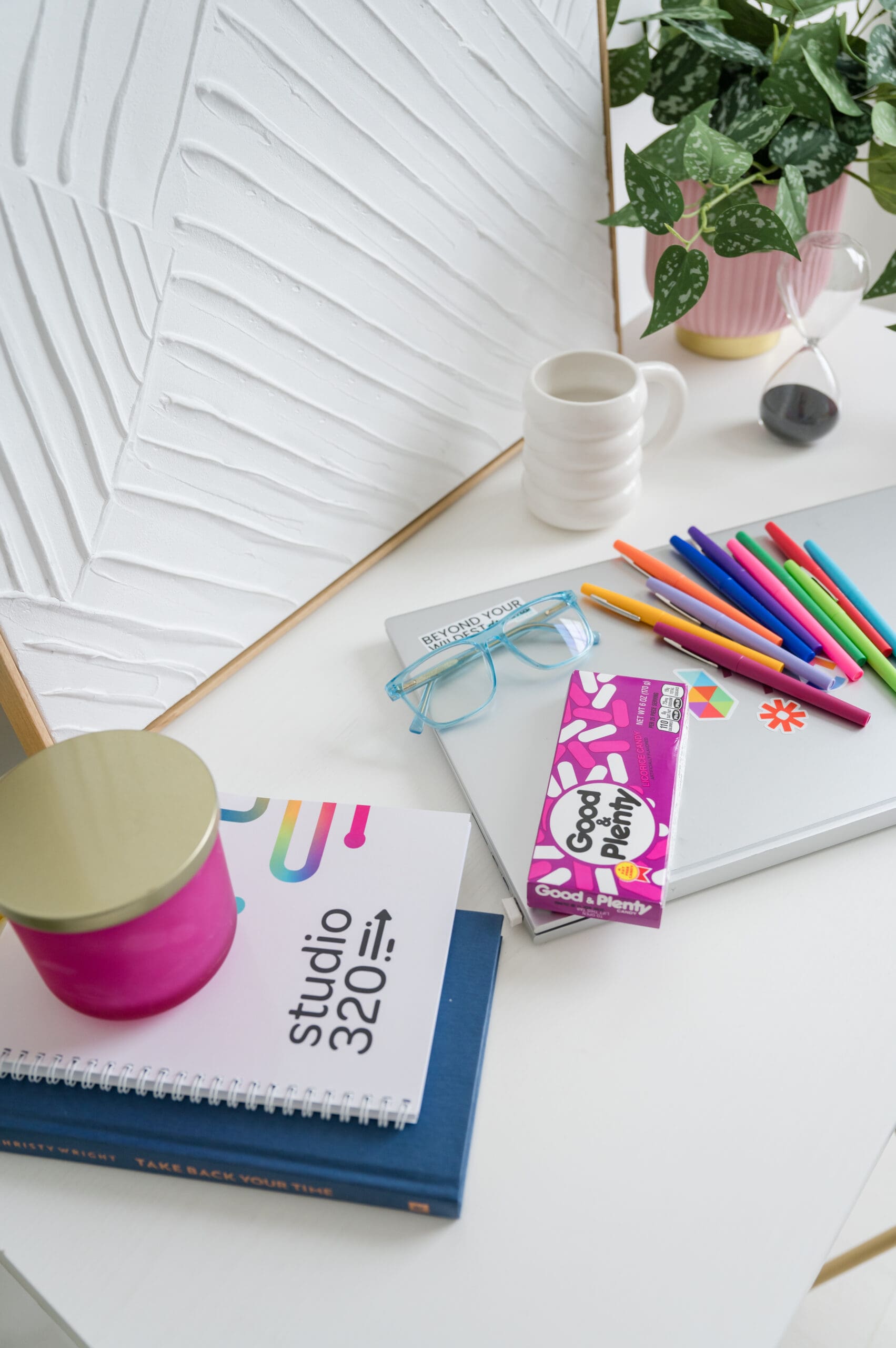 Bright and colorful desktop workspace featuring Studio320 branding, a laptop with vibrant pens, Good & Plenty candy, glasses, a coffee mug, and a plant—capturing a fun and organized vibe for creative entrepreneurs.